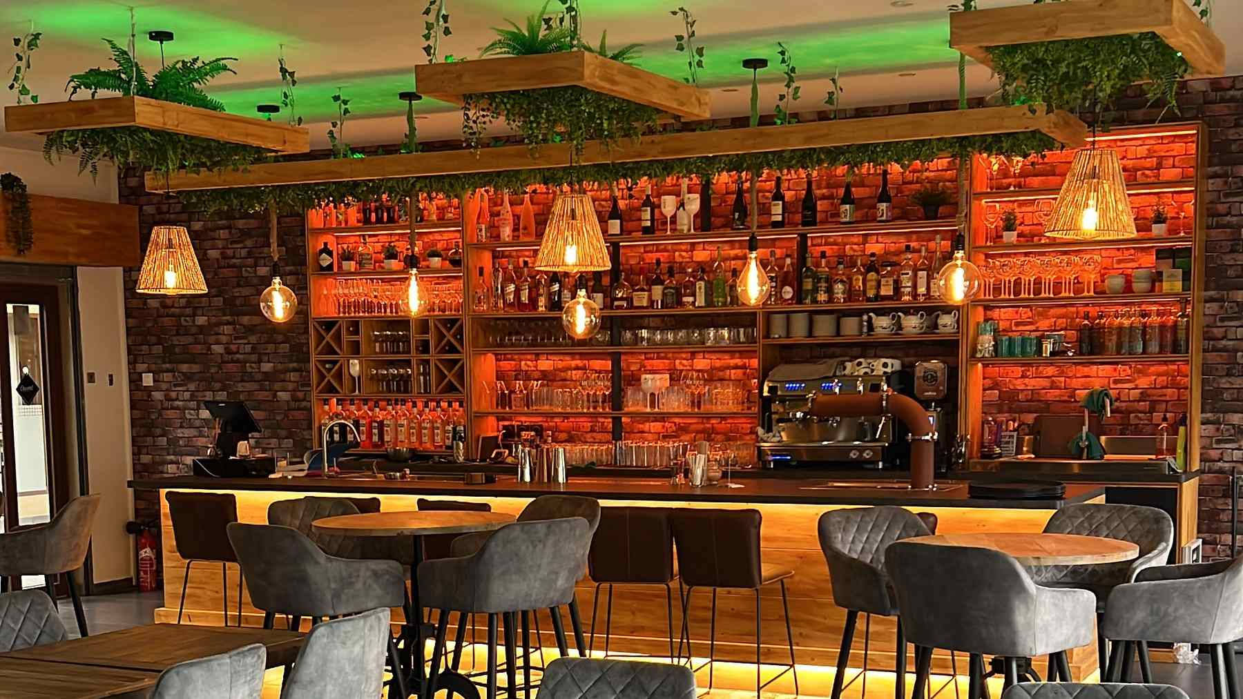La salle du restaurant Appa Lanka : tables en bois, fauteuils en velours et bar éclairé sous des plantes suspendues